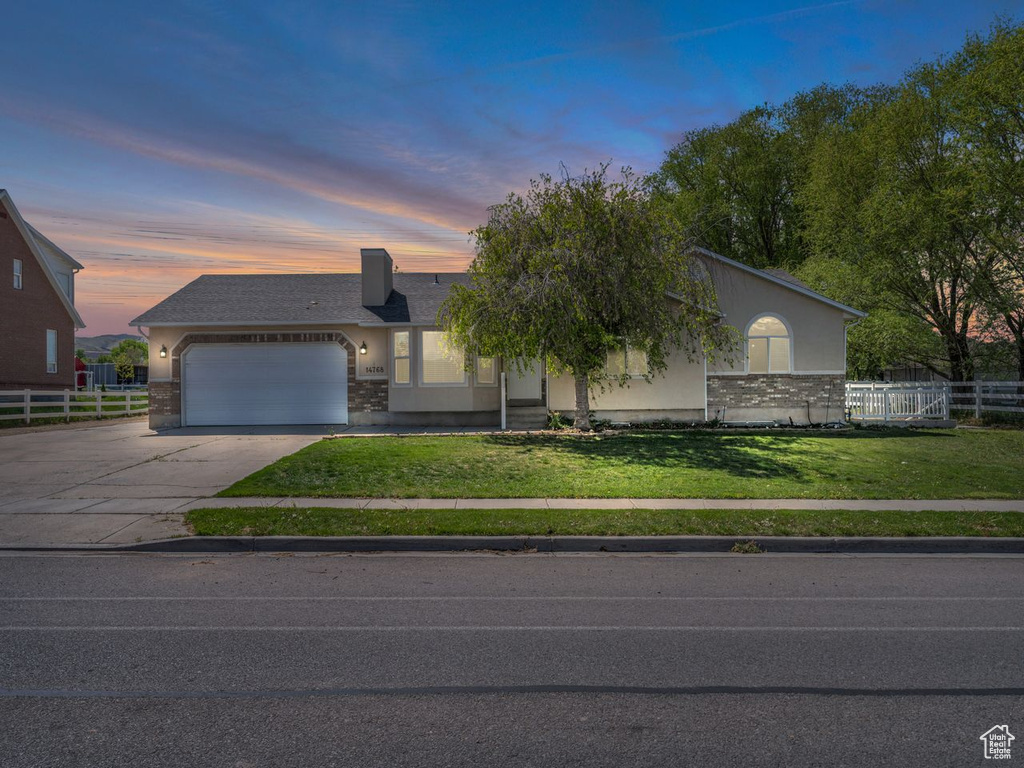 View of front facade with a yard, driveway, fence, a garage, and stucco siding