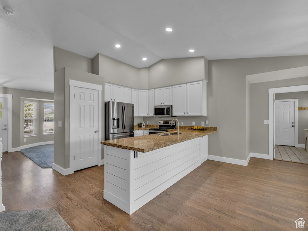 Kitchen with a peninsula, lofted ceiling, dark stone counters, baseboards, and appliances with stainless steel finishes
