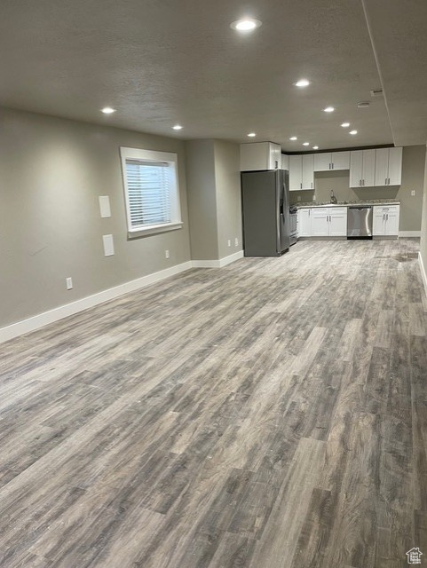 Unfurnished living room featuring wood finished floors, baseboards, a sink, and recessed lighting