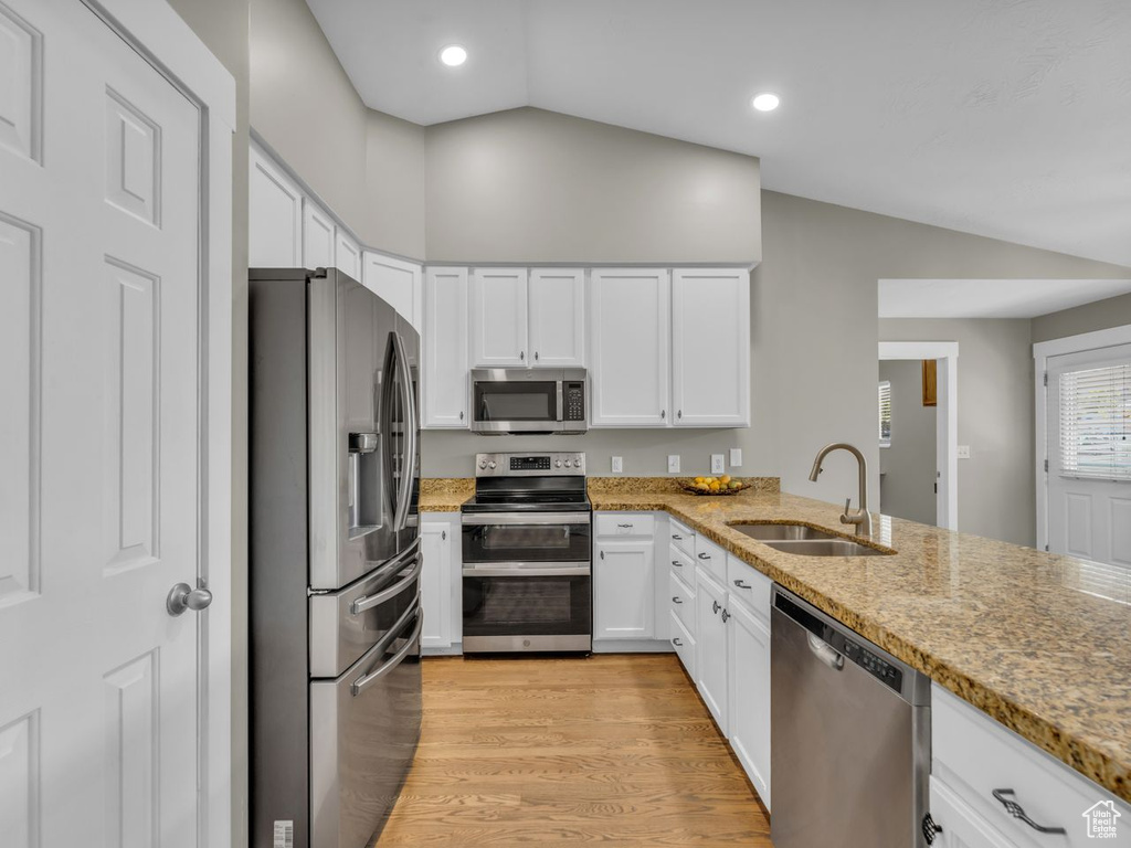 Kitchen featuring a sink, lofted ceiling, stainless steel appliances, light wood finished floors, and white cabinets