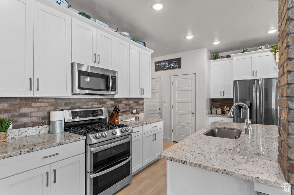 Kitchen with appliances with stainless steel finishes, a sink, light wood-style flooring, decorative backsplash, and white cabinetry