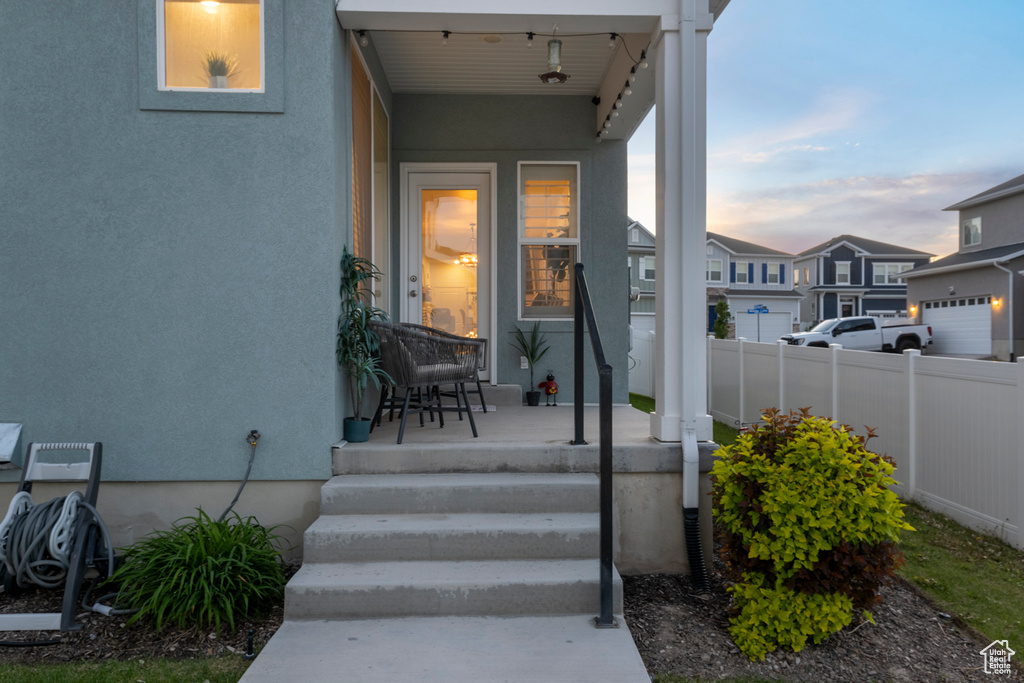 Property entrance with covered porch, stucco siding, and fence