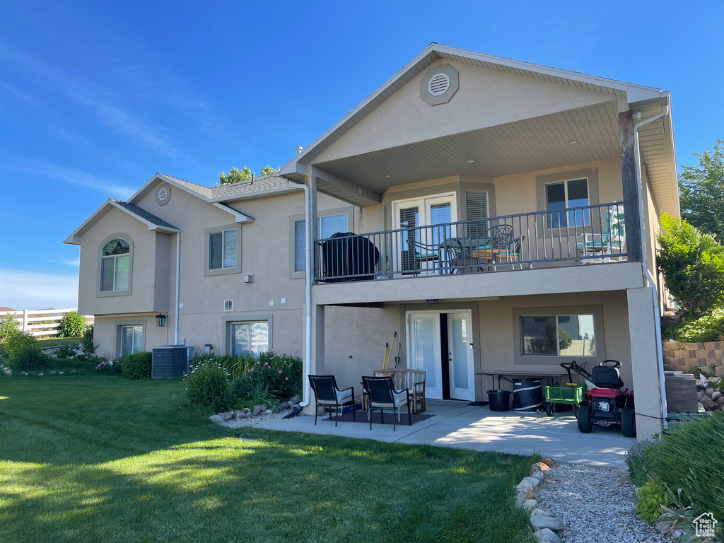 Rear view of house with a balcony, stucco siding, a patio, a lawn, and central AC unit