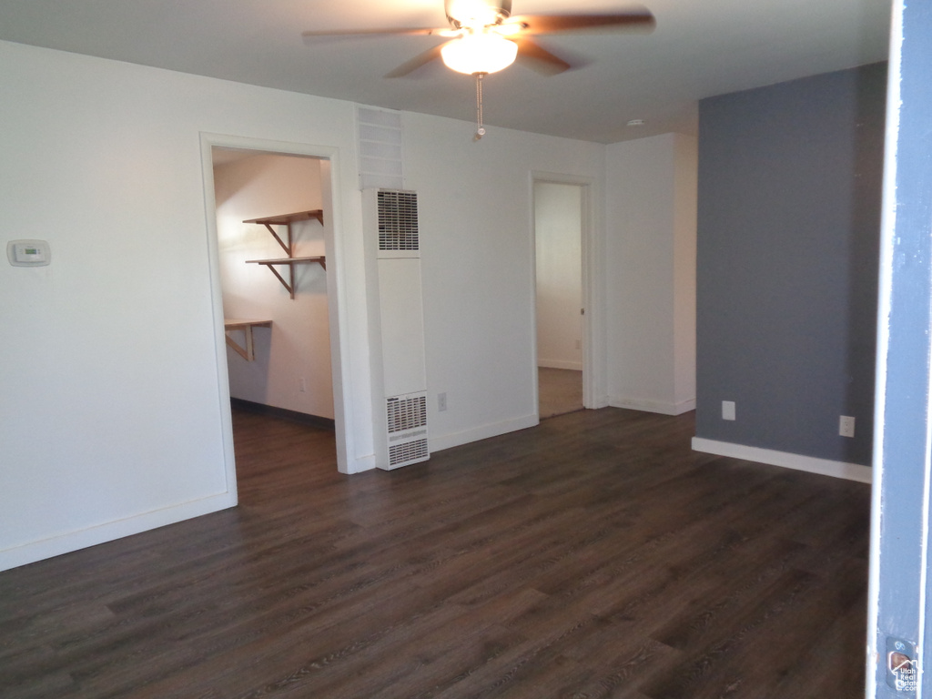 Unfurnished room featuring a heating unit, a ceiling fan, dark wood-type flooring, and baseboards