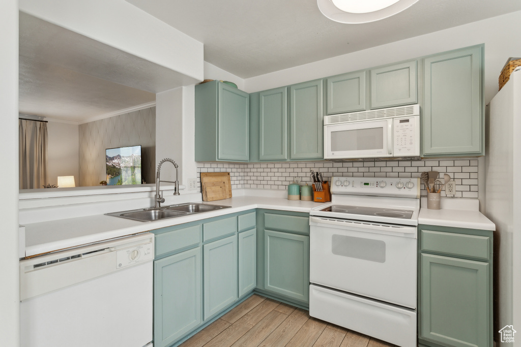 Kitchen featuring light wood-style floors, tasteful backsplash, a sink, and white appliances