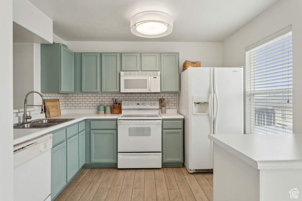 Kitchen featuring white appliances, a sink, green cabinetry, and light wood finished floors