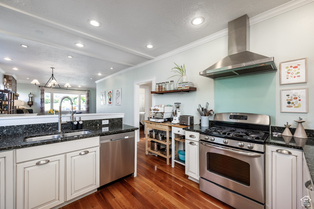 Kitchen featuring appliances with stainless steel finishes, wall chimney range hood, a sink, ornamental molding, and dark wood-style flooring