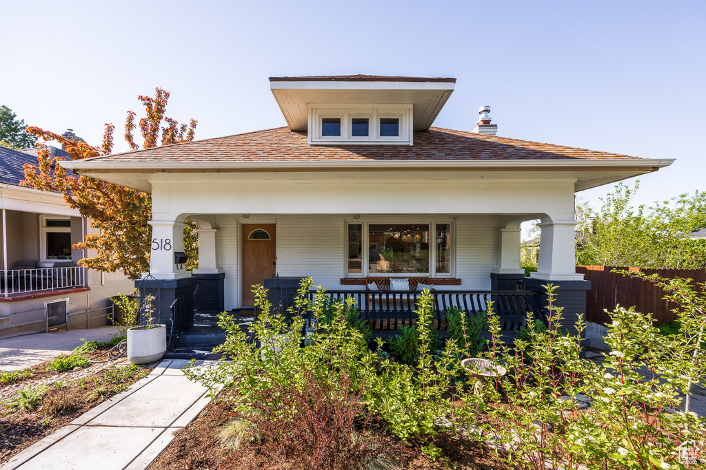 View of front of house featuring covered porch, brick siding, a shingled roof, and a chimney