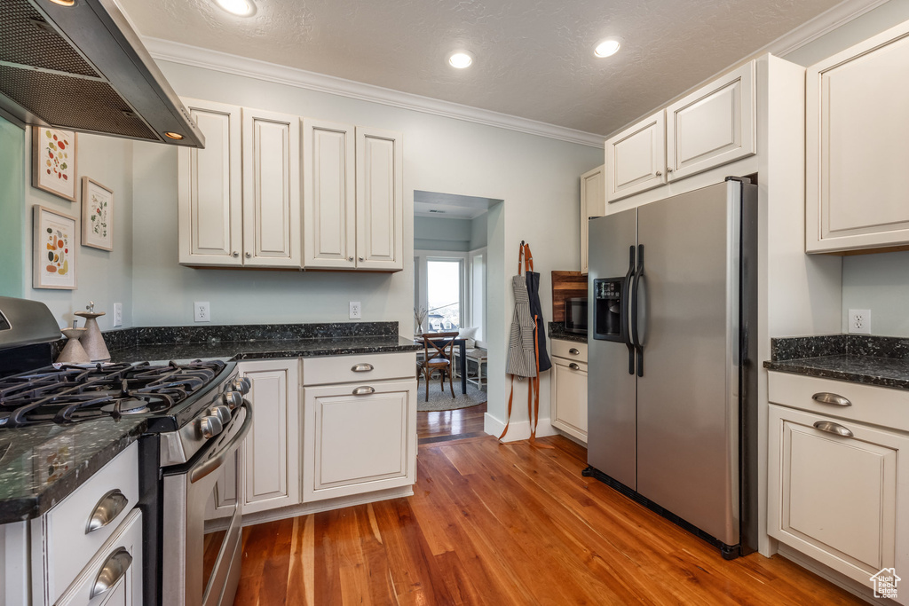Kitchen with stainless steel appliances, range hood, light wood-style flooring, crown molding, and recessed lighting