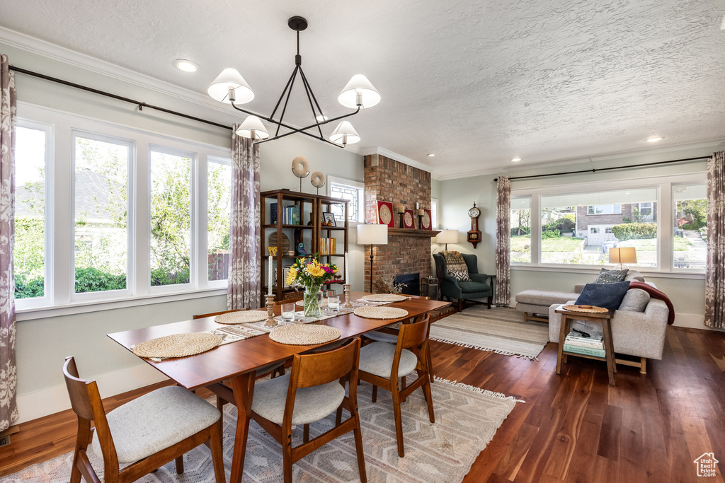 Dining room with a textured ceiling, crown molding, a fireplace, a chandelier, and dark wood-type flooring