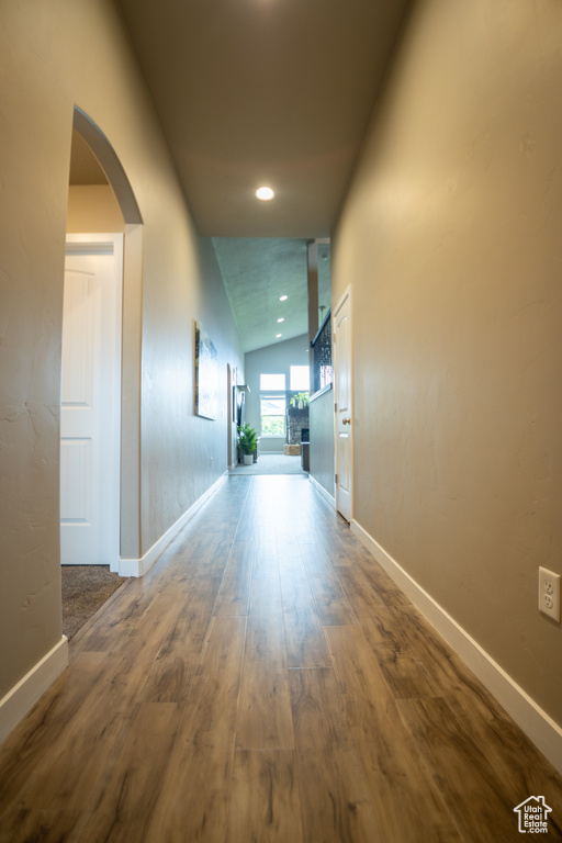 Hallway with arched walkways, wood finished floors, vaulted ceiling, baseboards, and recessed lighting
