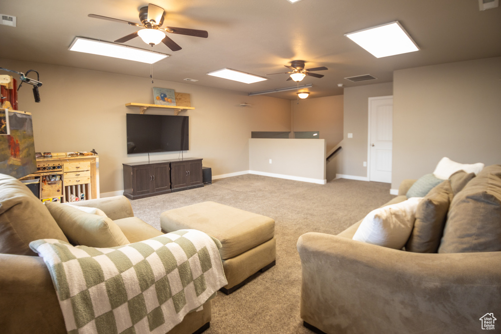Living room with a ceiling fan, carpet flooring, baseboards, and a skylight