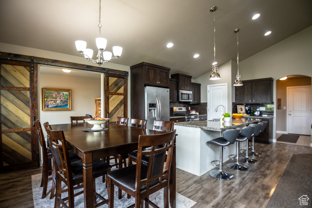 Dining room with a barn door, arched walkways, dark wood-style flooring, vaulted ceiling, and recessed lighting