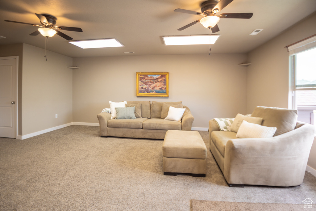 Carpeted living room with a skylight, ceiling fan, and baseboards