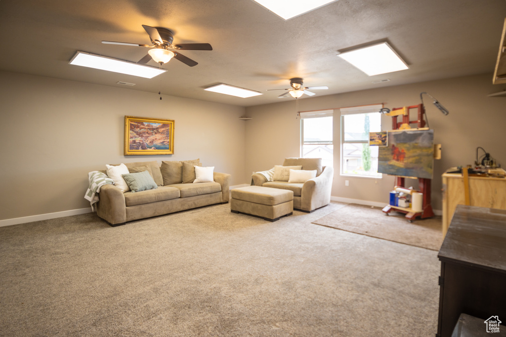 Carpeted living area with ceiling fan, a skylight, and baseboards