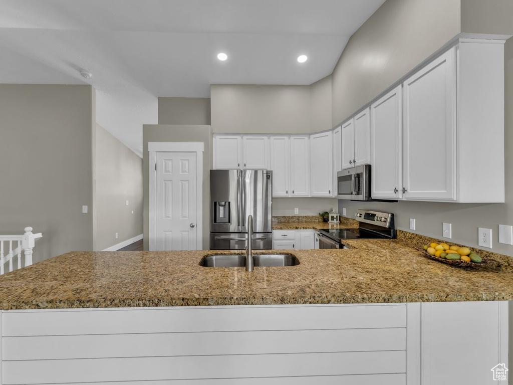 Kitchen with a sink, a peninsula, light stone counters, and appliances with stainless steel finishes