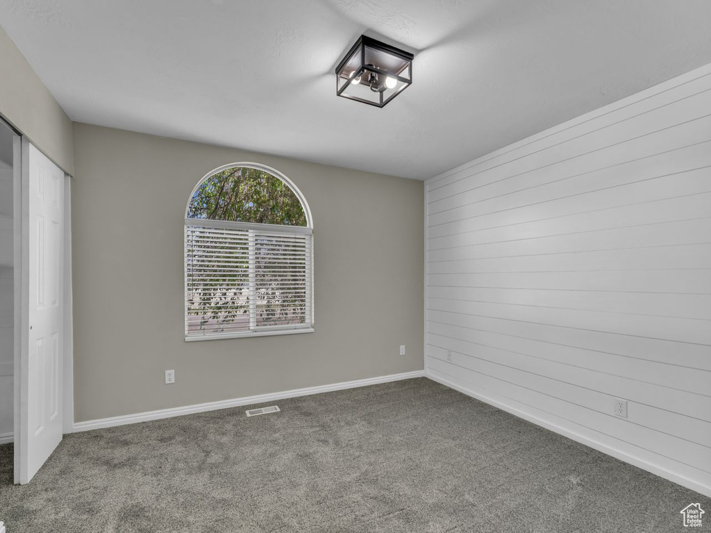 Carpeted empty room with baseboards, wood walls, and visible vents