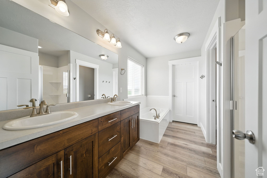 Bathroom featuring a bath, double vanity, wood finished floors, a shower stall, and a textured ceiling
