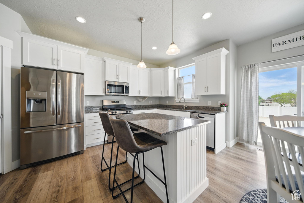 Kitchen featuring stainless steel appliances, a sink, a kitchen island, white cabinets, and recessed lighting