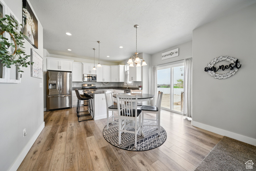 Dining area with a chandelier, baseboards, light wood-type flooring, recessed lighting, and a textured ceiling
