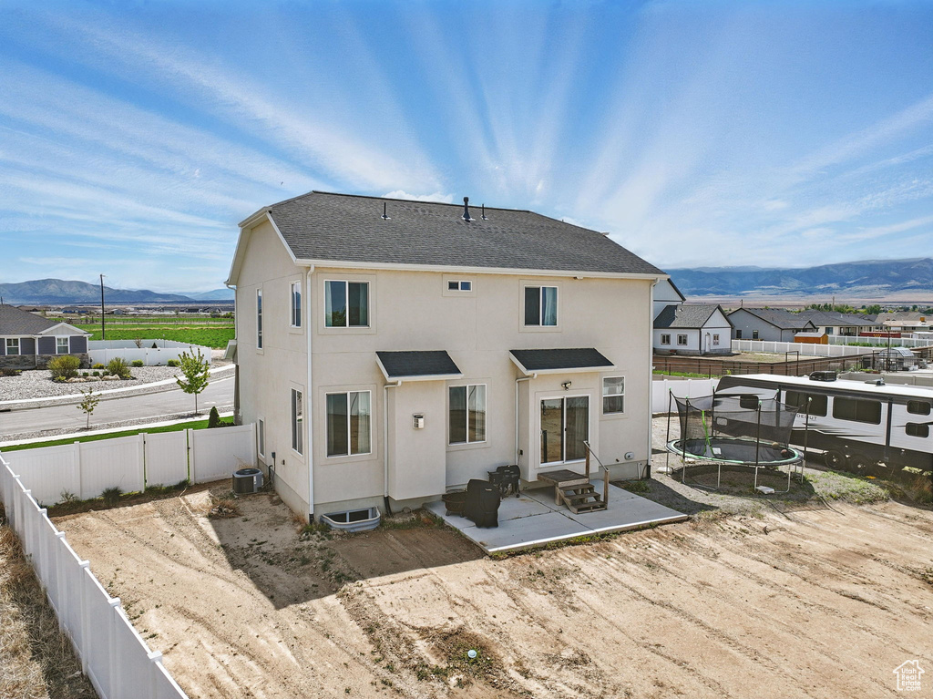 Rear view of house featuring a trampoline, a patio area, a mountain view, a fenced backyard, and stucco siding