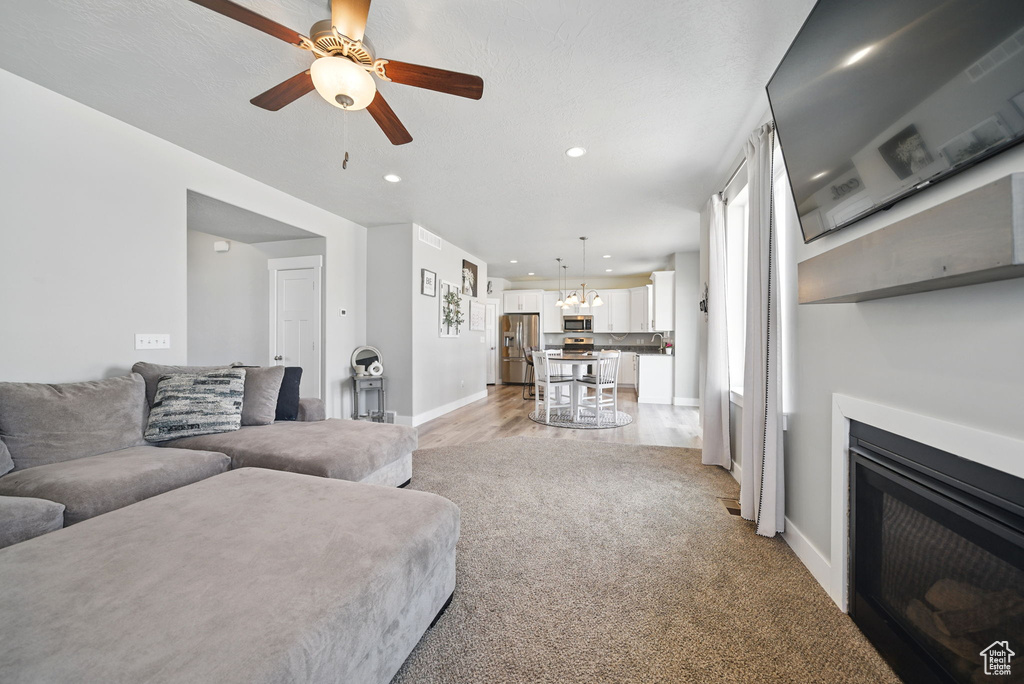Living room with baseboards, a ceiling fan, recessed lighting, a fireplace, and a chandelier