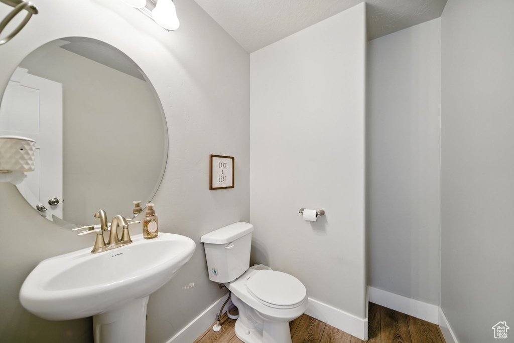 Half bathroom with toilet, wood finished floors, baseboards, and a sink
