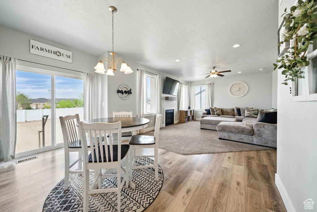 Dining space featuring a textured ceiling, light wood-style flooring, a chandelier, baseboards, and a glass covered fireplace