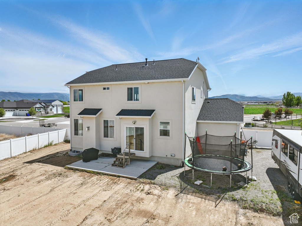 Rear view of house with a trampoline, a patio, fence, a mountain view, and stucco siding