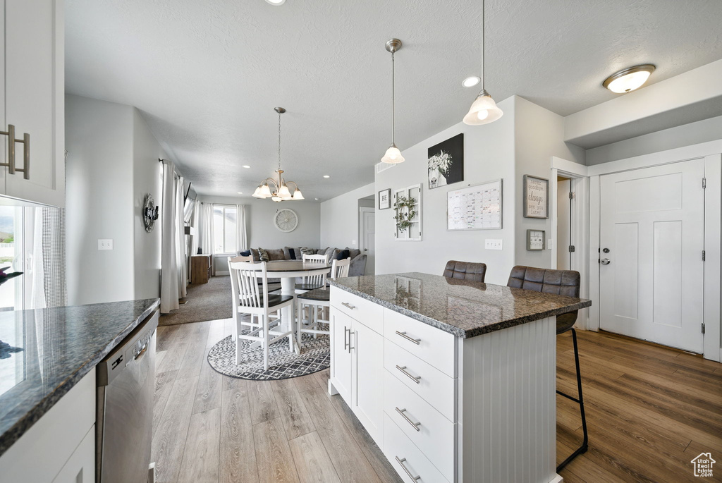 Kitchen featuring stainless steel dishwasher, a kitchen bar, wood finished floors, a chandelier, and white cabinets