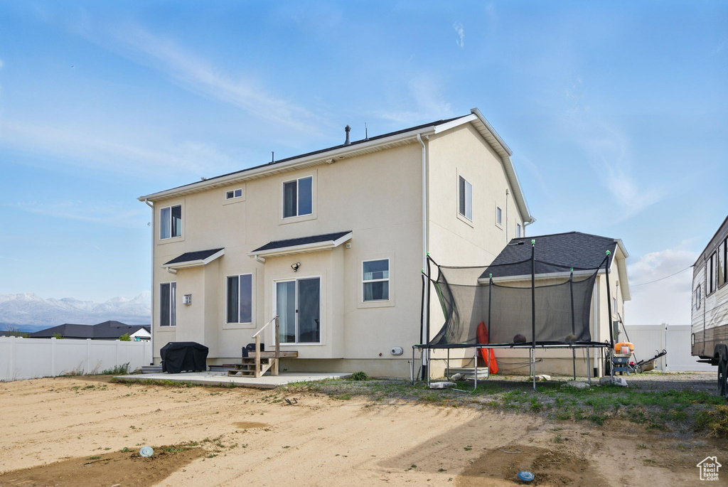 Back of property with entry steps, a trampoline, fence, stucco siding, and a patio