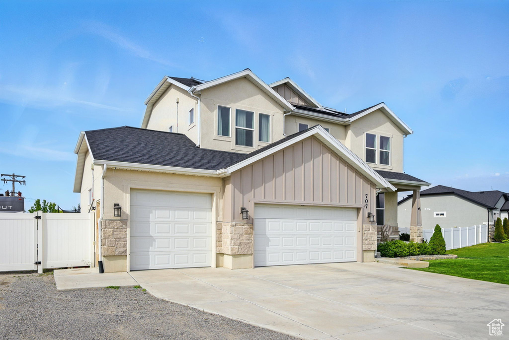 View of front of home with stone siding, fence, a garage, and concrete driveway