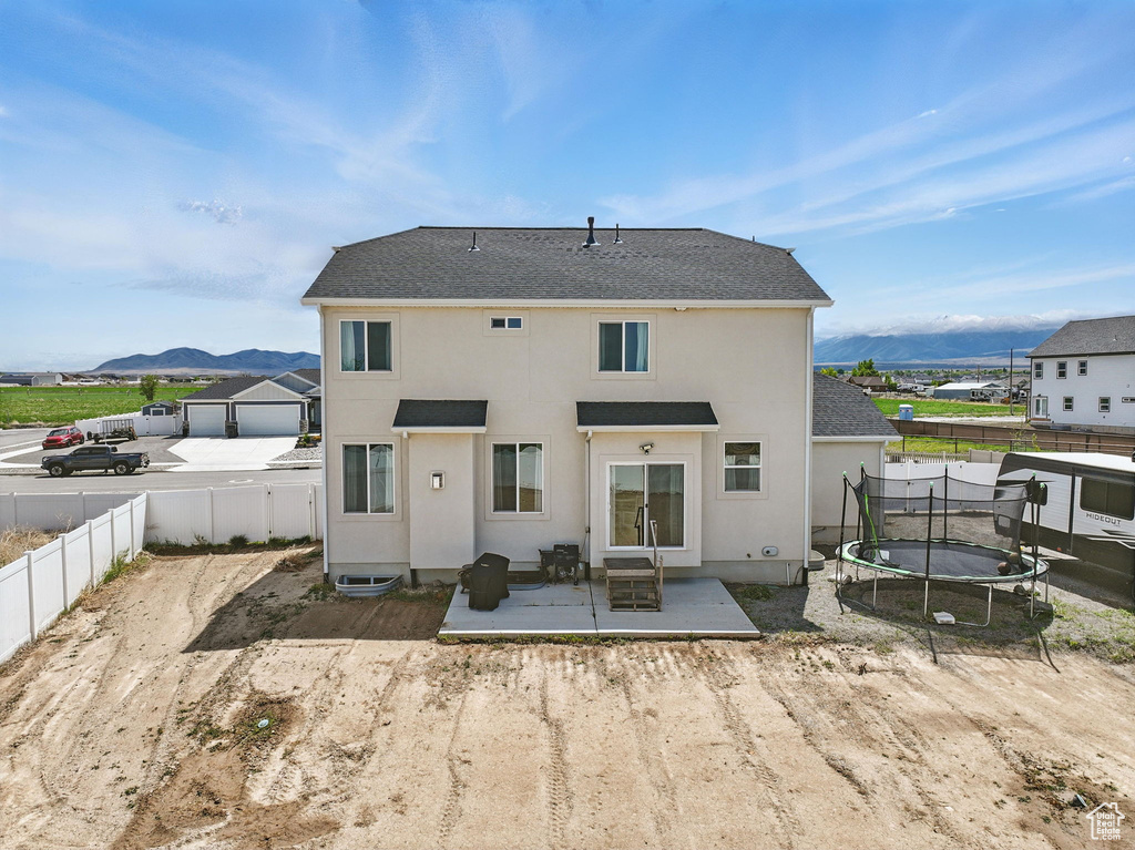 Rear view of property with a trampoline, a patio, a mountain view, a fenced backyard, and stucco siding