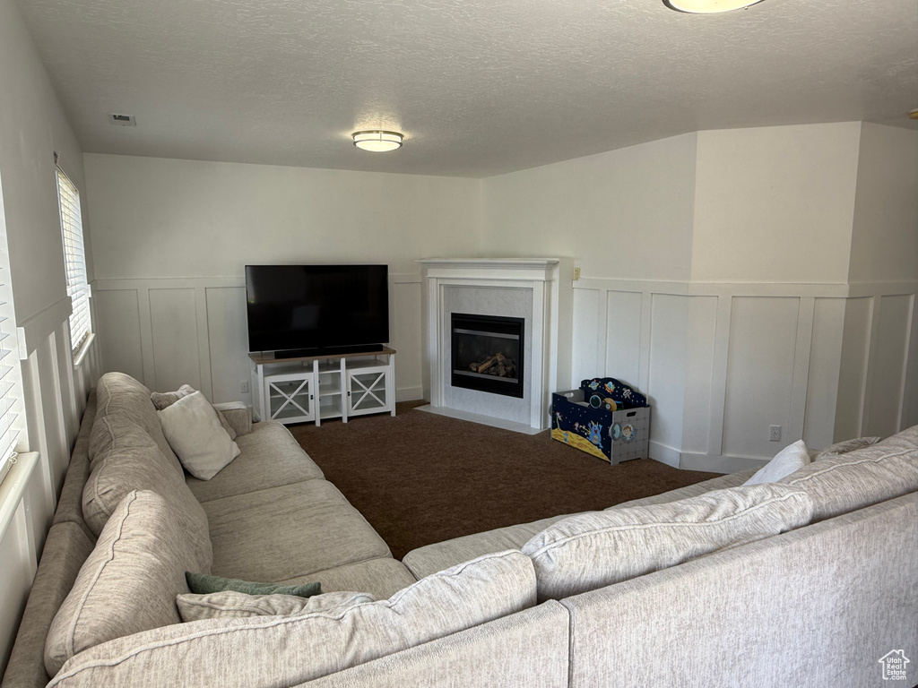 Living area featuring a fireplace with flush hearth, a decorative wall, carpet, a textured ceiling, and wainscoting