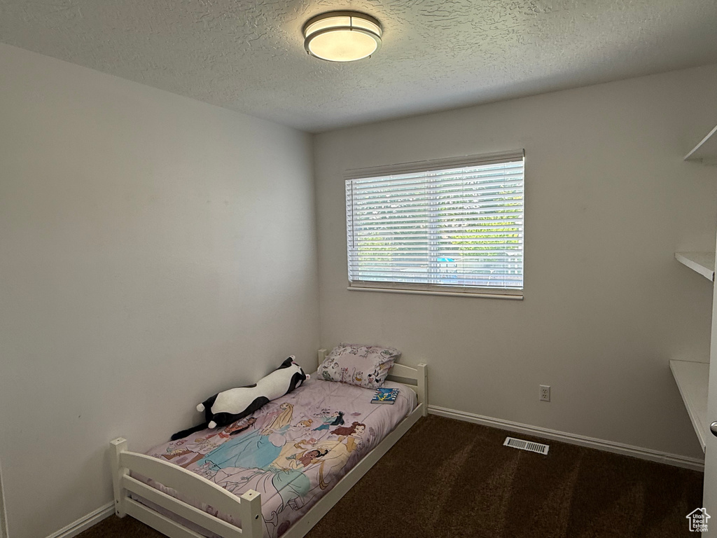 Bedroom with a textured ceiling, baseboards, and dark carpet