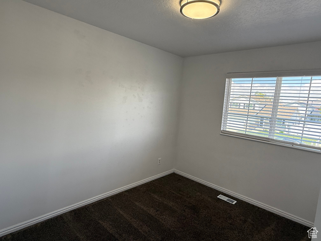 Empty room featuring baseboards, dark carpet, and a textured ceiling