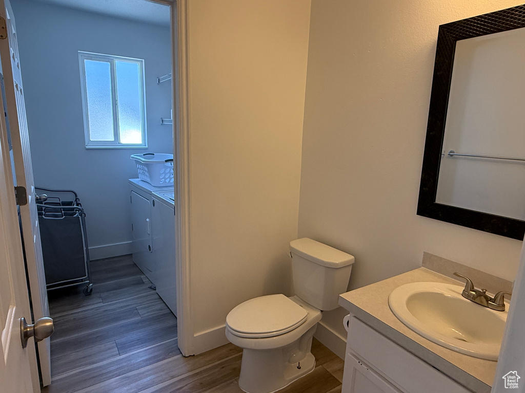 Bathroom with washing machine and clothes dryer, vanity, wood finished floors, toilet, and baseboards