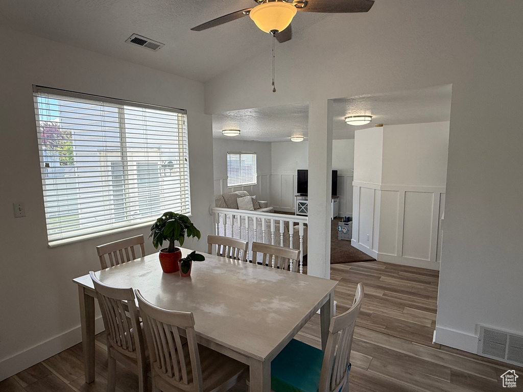 Dining area with wood finished floors, a ceiling fan, vaulted ceiling, wainscoting, and a decorative wall