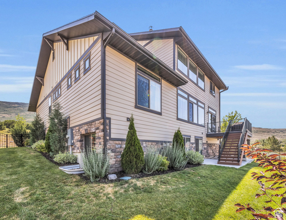 View of side of home featuring board and batten siding, a yard, fence, stone siding, and stairs