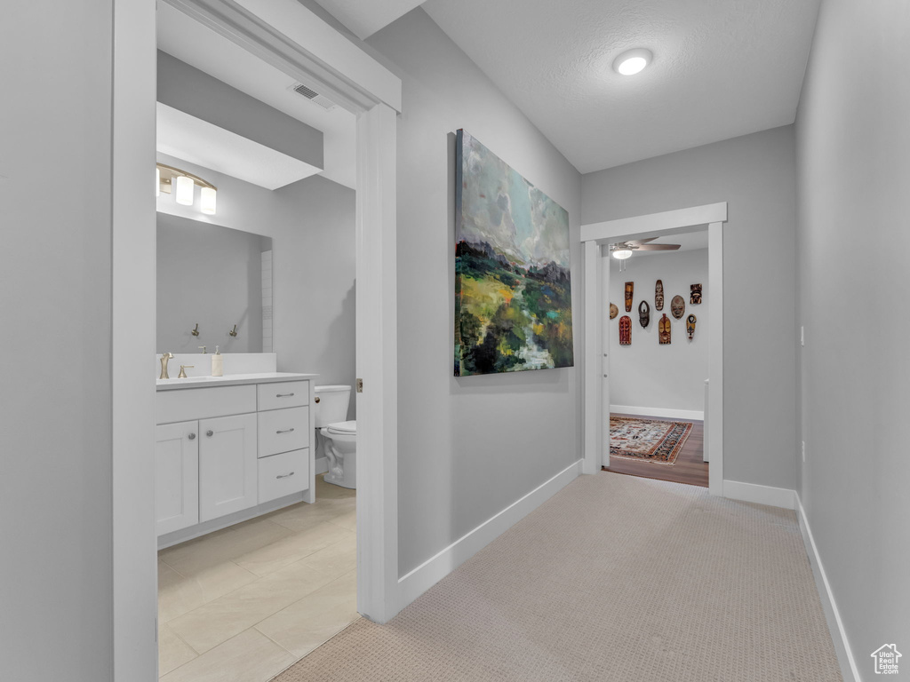 Hallway featuring a textured ceiling, a sink, visible vents, baseboards, and light tile patterned flooring