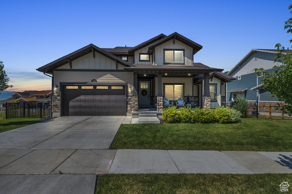 Craftsman-style home with covered porch, fence, driveway, a front yard, and an attached garage