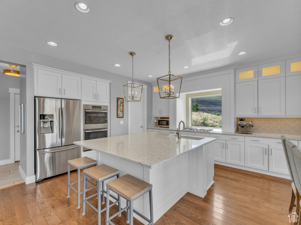 Kitchen with a notable chandelier, white cabinets, stainless steel appliances, and tasteful backsplash