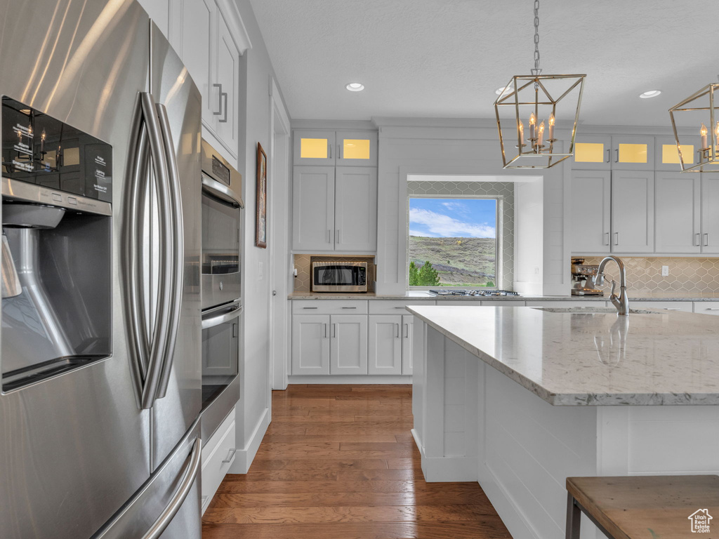 Kitchen with recessed lighting, a chandelier, decorative backsplash, glass insert cabinets, and appliances with stainless steel finishes