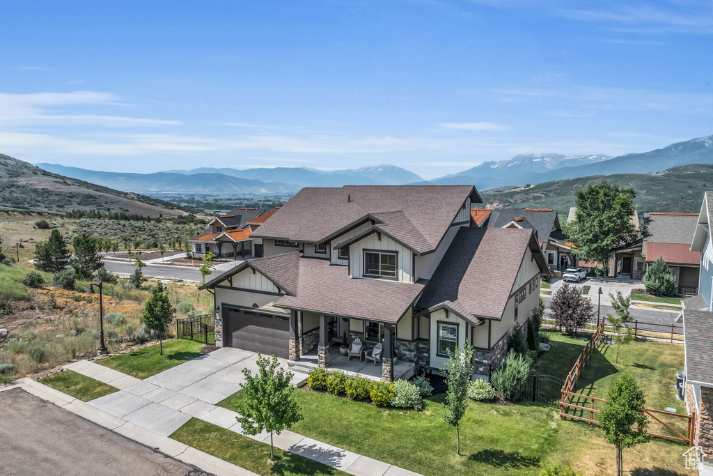 View of front of house featuring a mountain view, roof with shingles, fence, and stone siding