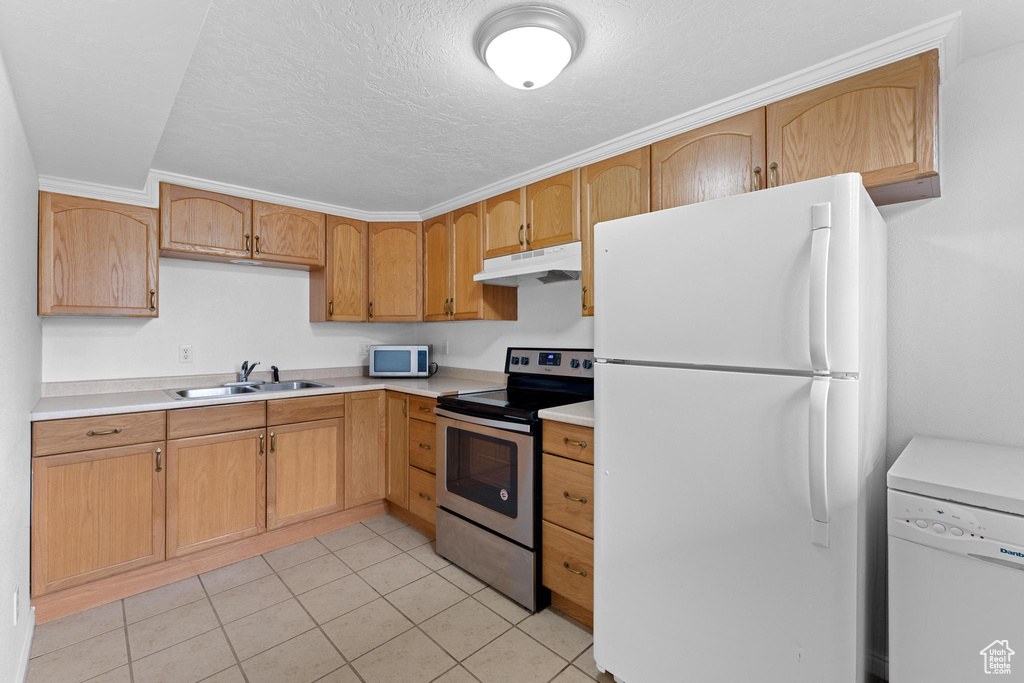 Kitchen featuring white appliances, under cabinet range hood, a sink, light countertops, and light tile patterned floors