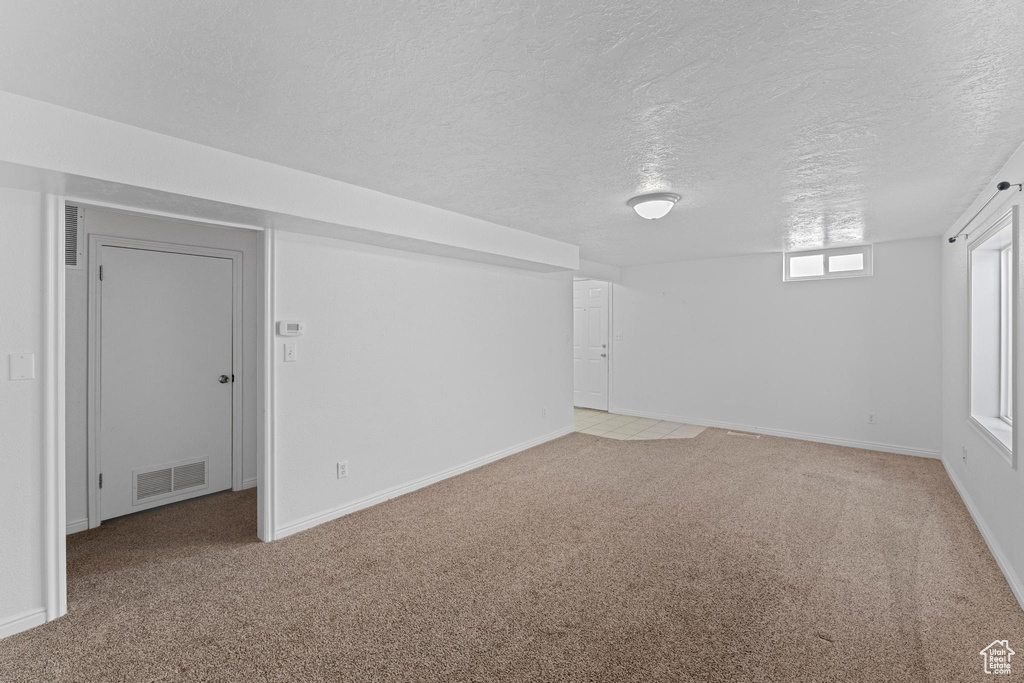 Below grade area with a textured ceiling, light colored carpet, and baseboards