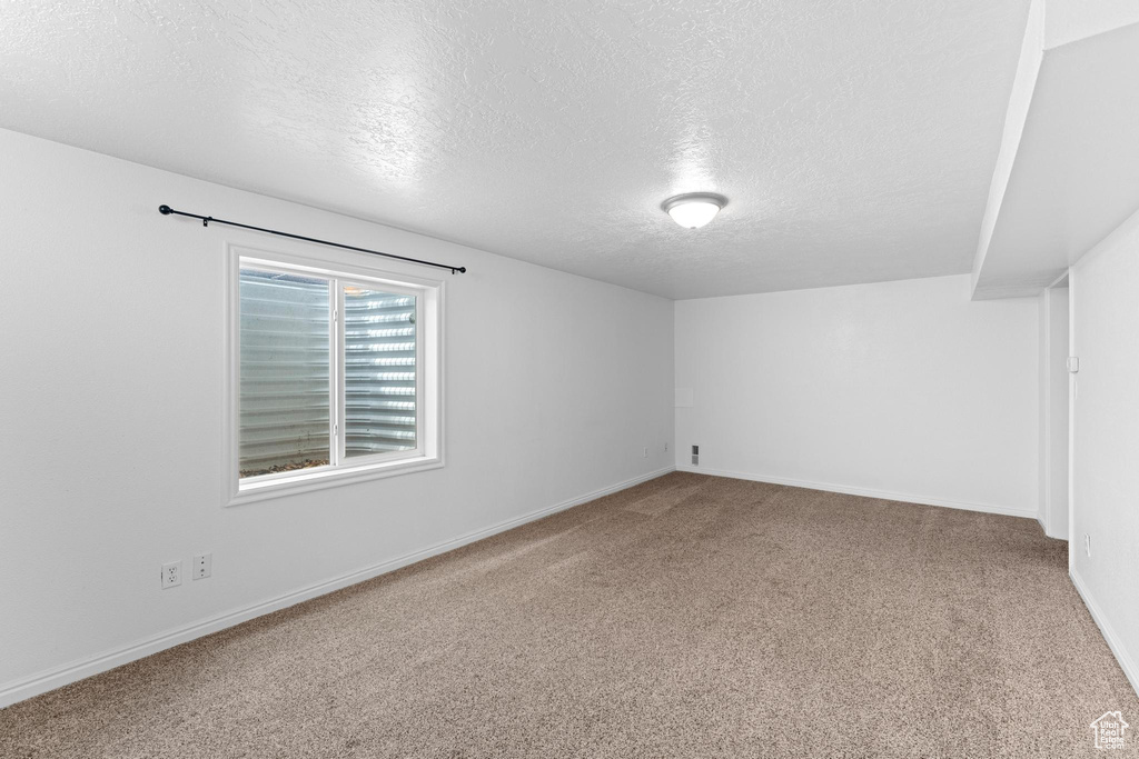Spare room featuring a textured ceiling, carpet flooring, and baseboards