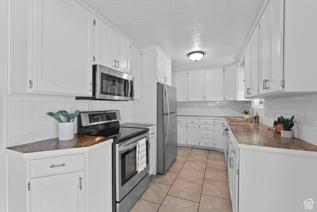 Kitchen featuring appliances with stainless steel finishes, a sink, a textured ceiling, white cabinetry, and dark countertops