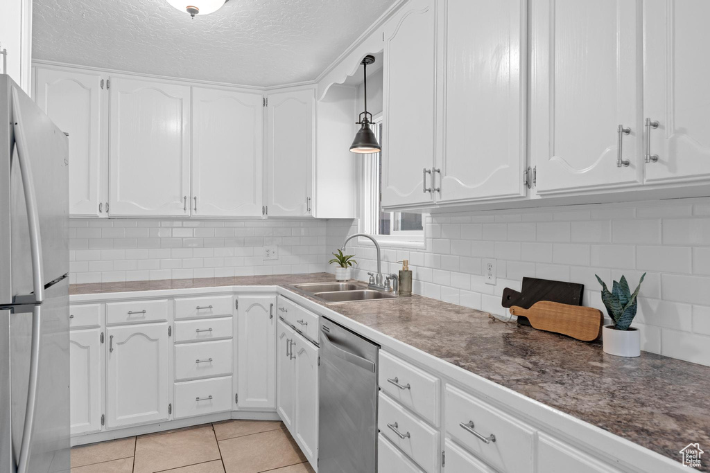 Kitchen with appliances with stainless steel finishes, a sink, white cabinets, backsplash, and pendant lighting