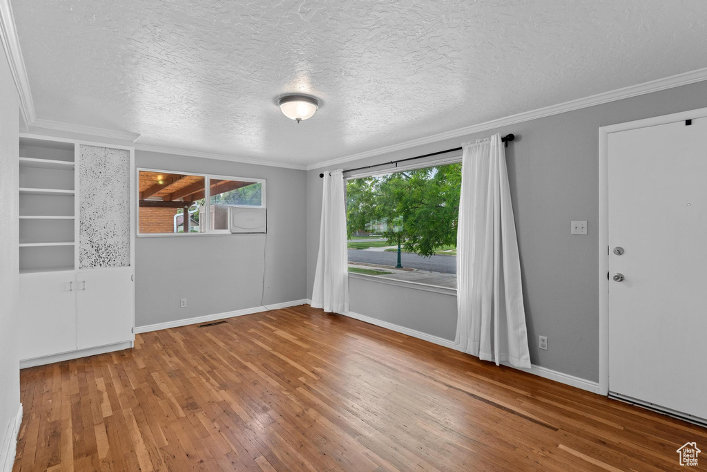 Unfurnished room featuring hardwood / wood-style floors, crown molding, a textured ceiling, and baseboards